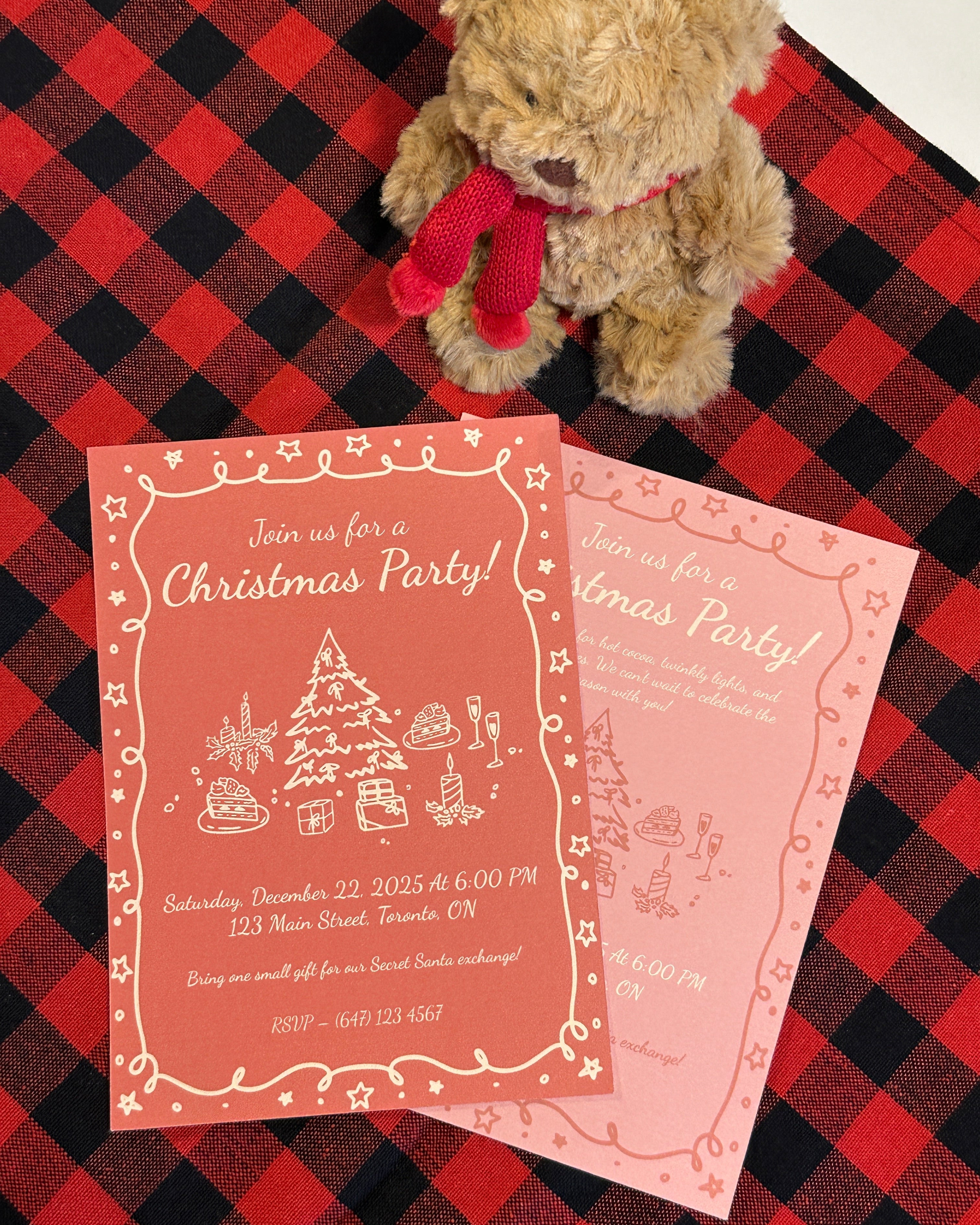 Two Christmas party invitations on a red and black checkered tablecloth with a teddy bear.